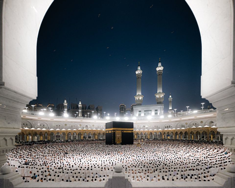 Masjidil Haram pada malam hari, Ka'bah dikelilingi jemaah, dilihat dari balik lengkungan
